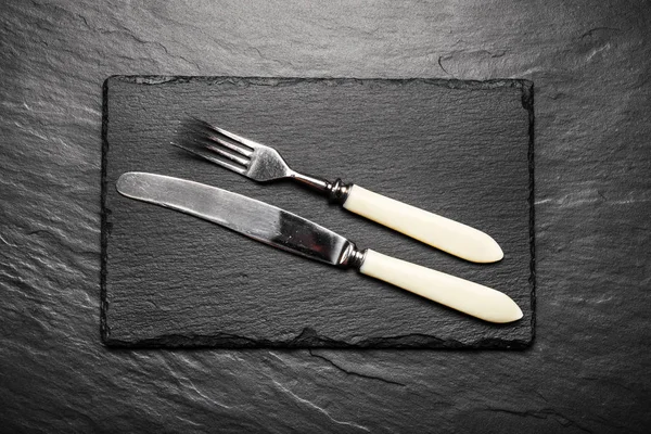 Black slate board for serving with fork and knife, top view — Stock Photo, Image