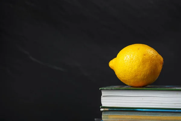 Limão amarelo deitado na pilha de livros sobre fundo preto — Fotografia de Stock