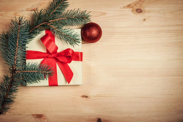 Vánoční dárek zabalený v červenou stuhou s větvičku jedle na dřevěné pozadí — Stock fotografie