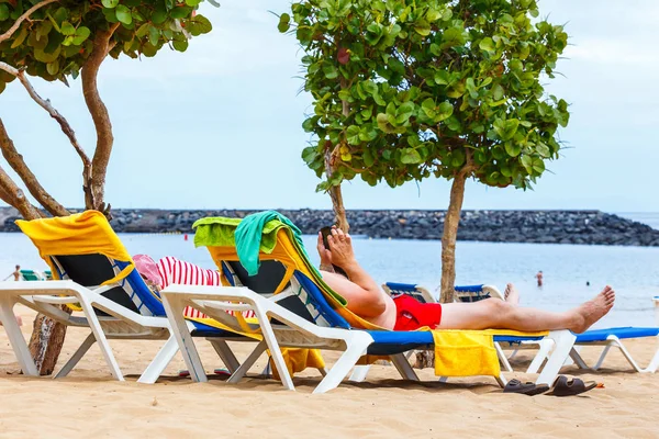 Un uomo non identificato su una sedia a sdraio con cellulare in spiaggia — Foto Stock