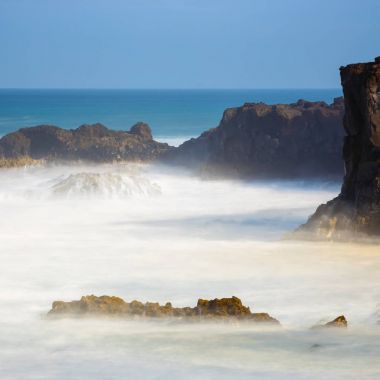 Los Hervideros, dalgalı okyanus ve mavi gökyüzü, uzun süreli pozlama ile volkanik kıyı şeridi