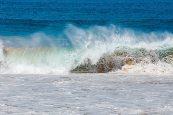 Blue wave crashes down at the beach in El Cotillo village in Fuerteventura island, Spain — стоковое фото