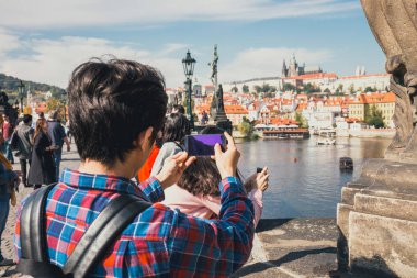 Prag, Çek Cumhuriyeti, 30 Eylül 2017: Genç adam fotoğraf onun smartphone ile Charles Köprüsü üzerinde güzel sonbahar gün boyunca, Prague, Çek Cumhuriyeti alıyor