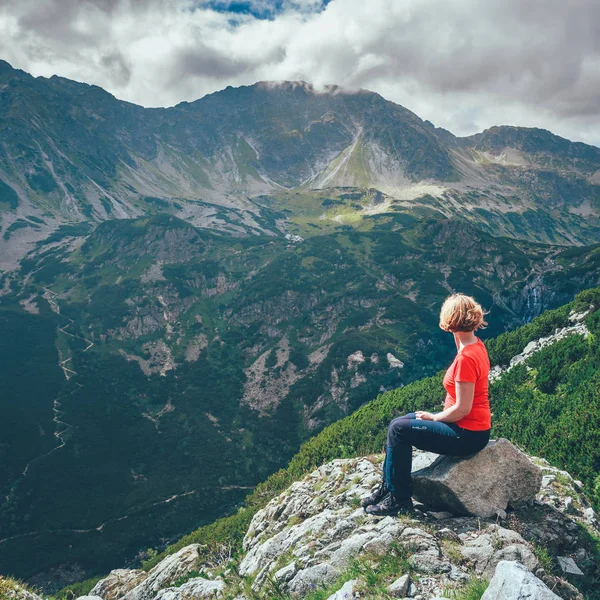 Vrouw zit op de klif en kijkt naar de toppen van bergen — Stockfoto