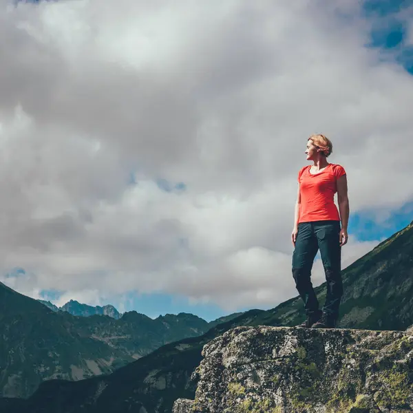 Vrouw staat op de rots en kijkt naar de toppen van bergen — Stockfoto
