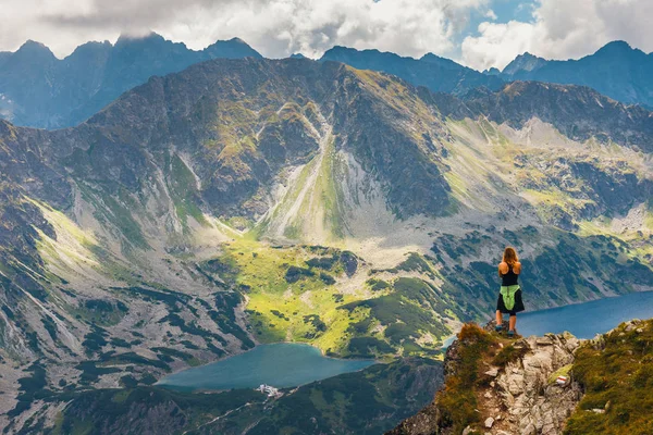 Mujer se para en el acantilado y mira a las cimas de las montañas —  Fotos de Stock