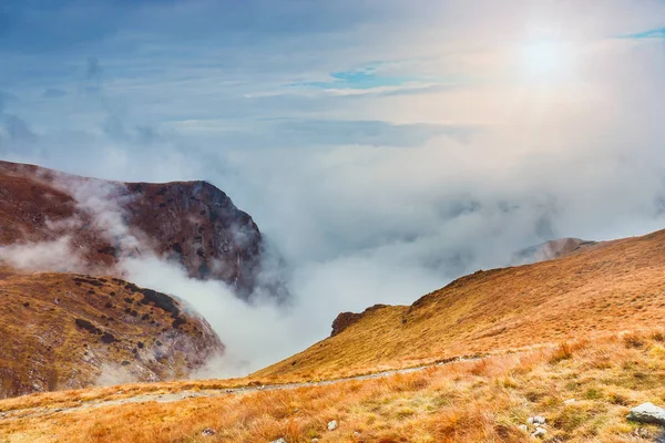 Berglandschap met mist onder de pieken en wolken boven hen in blauwe tinten — Stockfoto