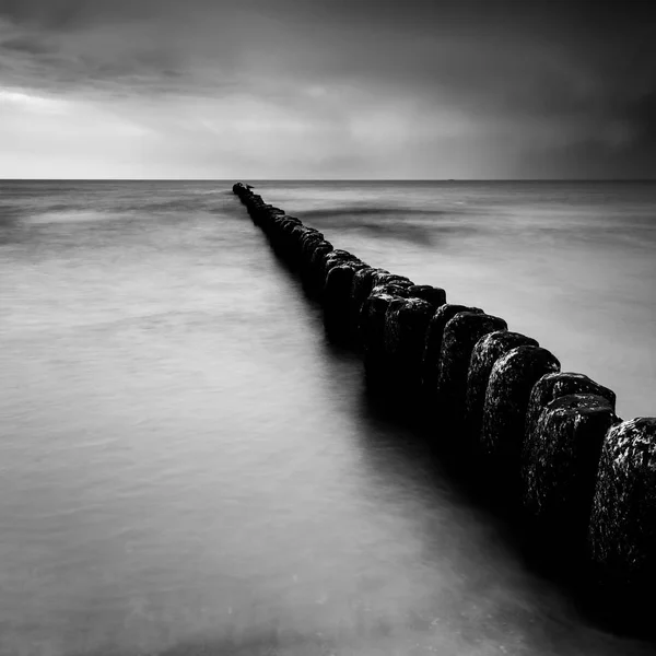 Закат над морем с деревянным пирсом, черно-белое фото, длительная экспозиция — стоковое фото