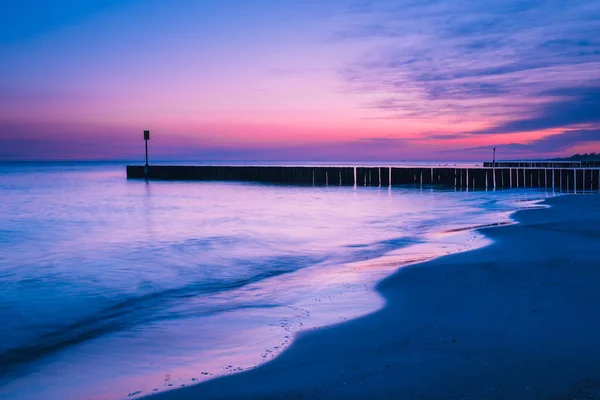 Puesta de sol en la playa con un rompeolas de madera, tono púrpura — Foto de Stock