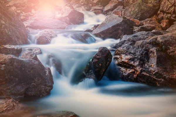 Schöner Wasserfall in den Bergen mit den Strahlen der Sonne, die durch die Bäume scheinen — Stockfoto