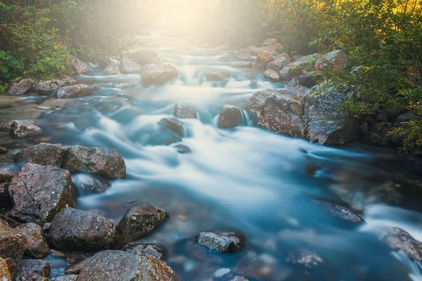 Belle cascade dans les montagnes avec les rayons du soleil qui brille à travers les arbres — Photo