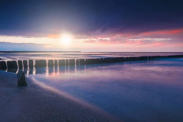 Puesta de sol en la playa con un rompeolas de madera, tono púrpura — Foto de Stock