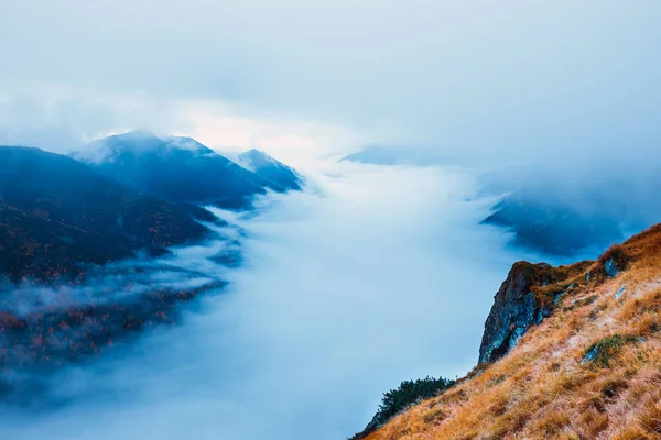 Mountain landscape with fog below the peaks and clouds above them in blue tones — Stock Photo, Image
