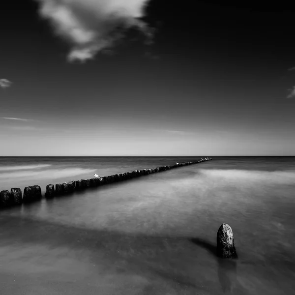 Puesta de sol sobre el mar con un muelle de madera, foto en blanco y negro, larga exposición — Foto de Stock