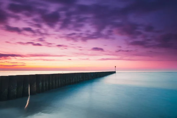 Puesta de sol en la playa con un rompeolas de madera, tono púrpura — Foto de Stock