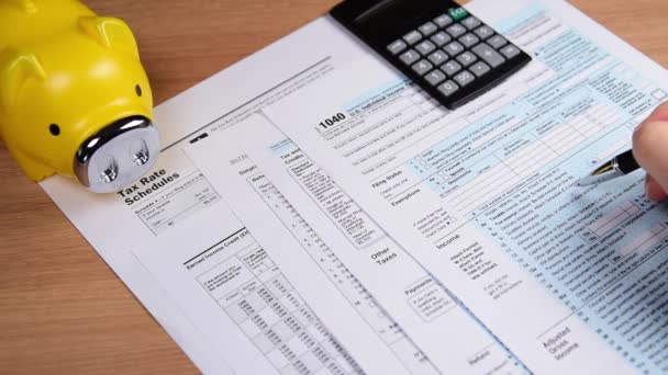 Formulario fiscal 1040, bolígrafo, alcancía y calculadora. sobre el escritorio . — Vídeo de stock