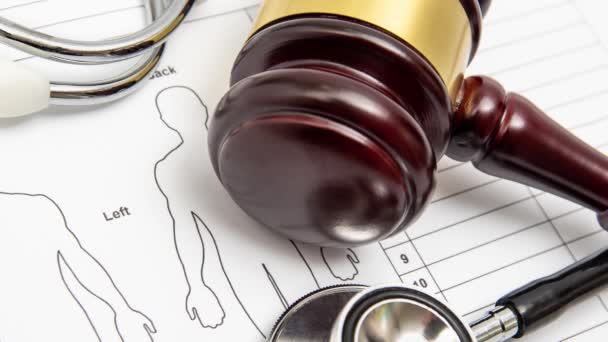 Oddálit. Dřevěný soudcův kladívko a stetoskop na lékařské kartě. Koncept medicínského sporu. — Stock video