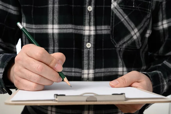 A close-up of a mans hand signing a document with a clipboard — Stok fotoğraf