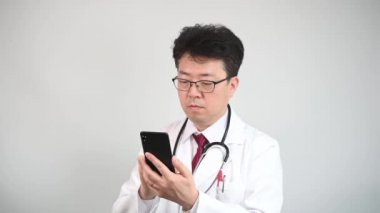 4 bin. Teletıp almak için akıllı telefon kullanan orta yaşlı Asyalı erkek doktor..