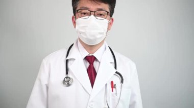 Ağır çekim. Orta yaşlı Asyalı bir erkek doktor beyaz maskeler takıyor ve termometre tavsiye ediyor..