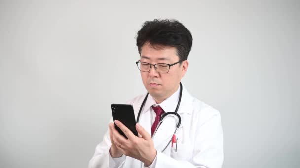 Μεσήλικας Ασιάτης Γιατρός Που Χρησιμοποιεί Ένα Smartphone Για Πάρει Τηλεϊατρική — Αρχείο Βίντεο