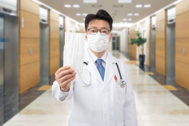 Orta yaşlı Asyalı doktor tek kullanımlık maskeyi elinde tutuyor..