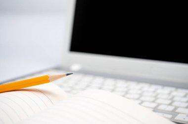 Çevrimiçi öğrenme kavramı. Dizüstü bilgisayarın klavyesinde çizgili bir defter ve sarı bir kalem var..