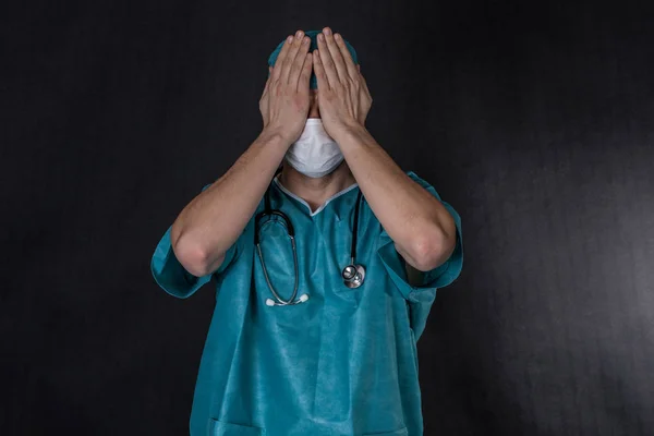 Хирург в халате, прикрывающий глаза. Чёрный фон — стоковое фото