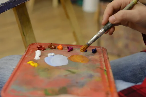 artist paints a picture of oil paint brush in hand with palette closeup