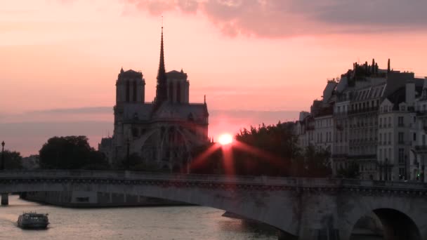 Un barco flotando frente a Notre Dame mientras el sol se pone en el fondo — Vídeos de Stock