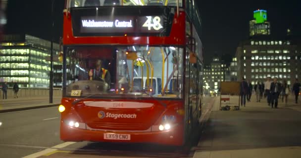 En röd London buss drar sig undan från en busshållplats i London på natten — Stockvideo