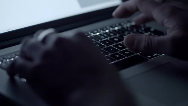 Sida på skott av en man att skriva på en bärbar dator i ett mörkt rum — Stockvideo