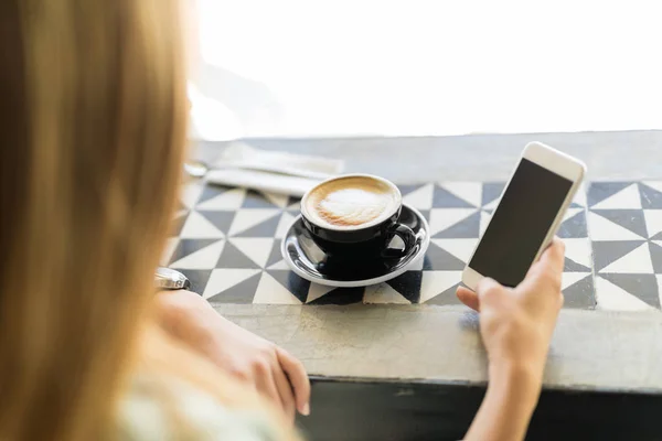 Kvinna med smartphone och dricka cappuccino — Stockfoto