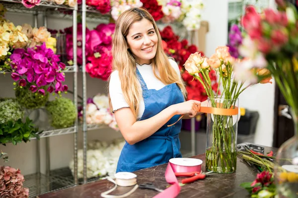 Young florist putting a ribbon on a glass vase — Stock Photo, Image