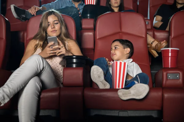 Woman checking phone at cinema with son — Stock Photo, Image