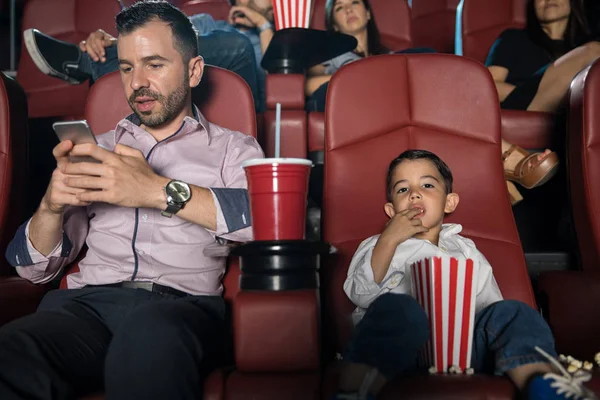 Homme vérifiant téléphone au cinéma avec son fils — Photo