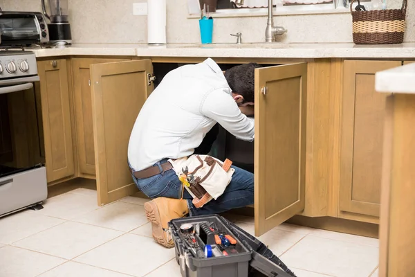 Loodgieter krijgen binnen een keukenkast — Stockfoto