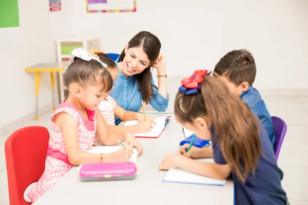 教室で書く練習と彼女の生徒たちを助けること幸せな幼稚園女性教師 — ストック写真