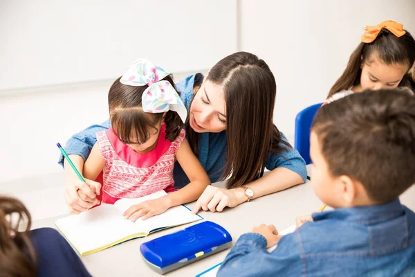 Pretty Young Preschool Teacher Tutoring One Her Pupils Writing Assignment — Stock Photo, Image