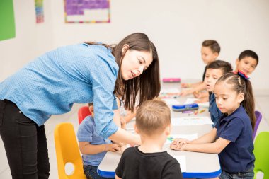 Sevimli kadın okul öncesi öğretmeni sabırla onun iş ödeve bir sınıfta onun öğrencilerinden açıklama