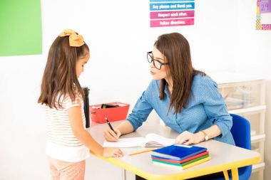 Gözlük takan ve onun öğrencilerinden masasında otururken çalışmaları sınıflandırma nerdy okul öncesi öğretmeni