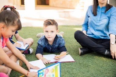 Çim üzerinde yalan ve okul öncesi sınıf açık havada alarak hoş beyaz çocuk portresi