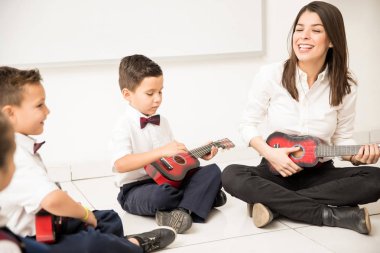 Grup okul öncesi öğrenci ve öğretmenleri müzik dersi olan ve bir sınıfta gitar çalmak
