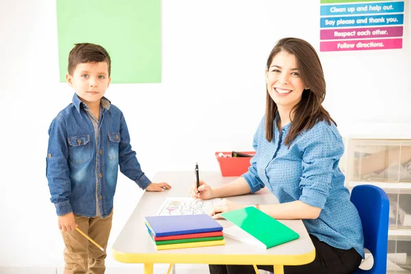 Attractive Hispanic Preschool Teacher Grading Student Work While Sitting Her — Stock Photo, Image