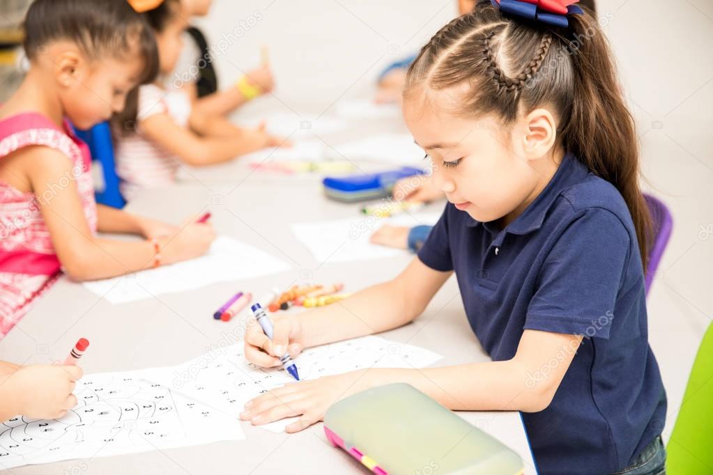 Portrait of a little girl doing a coloring activity with the rest of the group in a preschool classroom