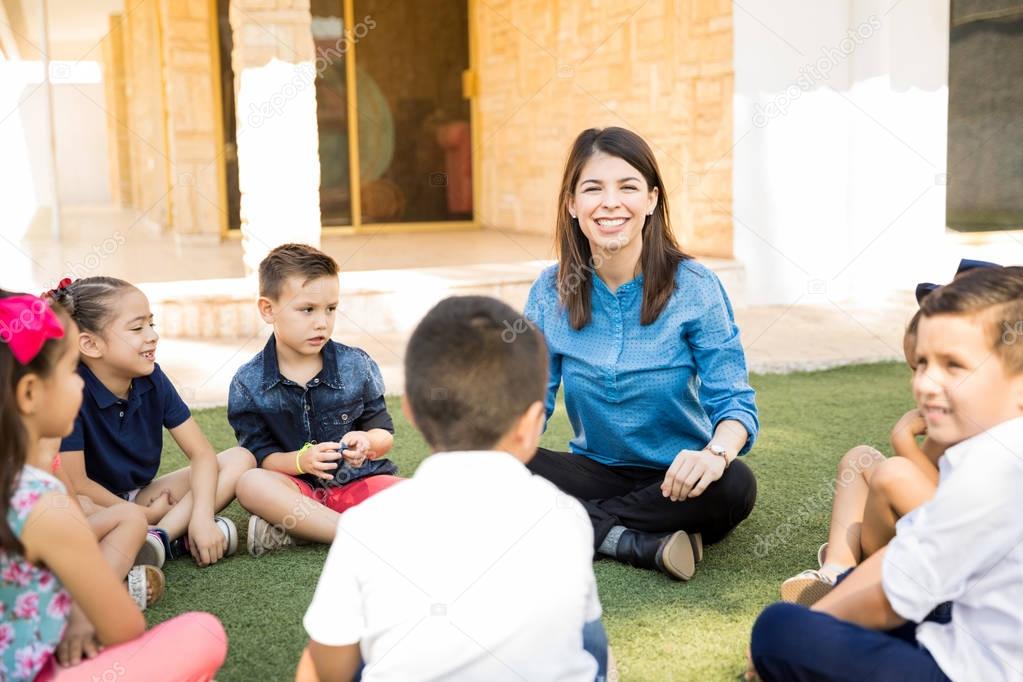 Portrait of a beautiful preschool teacher having a class outdoors with a group of students and smiling