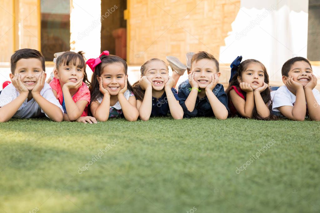 Portrait of a group of Hispanic preschool students lying on the grass outdoors and smiling