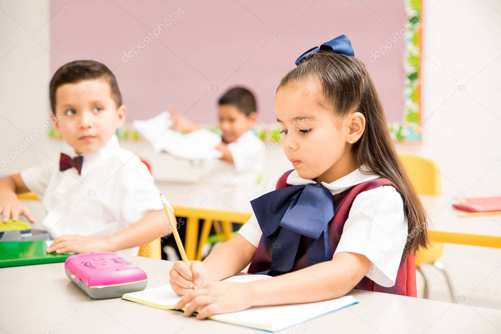 Cute preschool students wearing a uniform and doing a writing assigment in a classroom