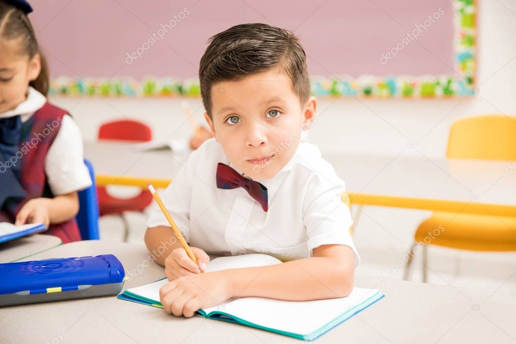 Good looking Latin preschooler in uniform paying attention to class and working on a writing assigment at school