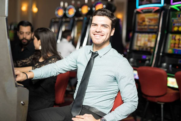 カジノでスロット マシンで遊んで 笑って楽しい時間を過ごす魅力的なラテン男の肖像 — ストック写真